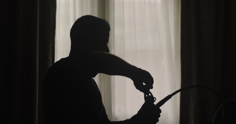A man turns a knob on a long hose in a dark room