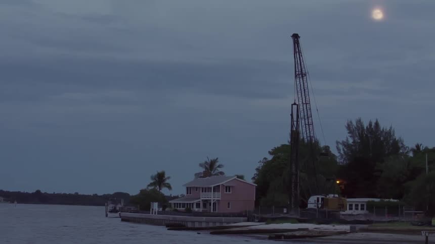 A view of houses, piers and a crane next to a body of water on a cloudy evening