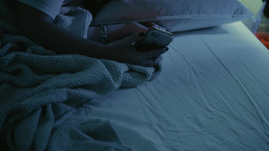 The person is holding their phone in the dark bedroom