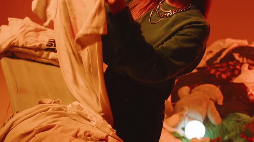 The woman is folding clothes on the ironing board as a man plays drums