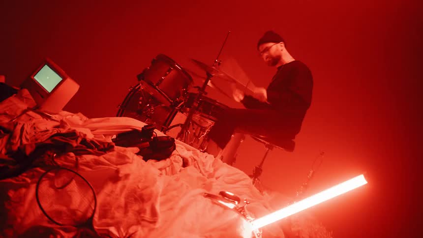 Man drums on a drum set surrounded by many objects and lights