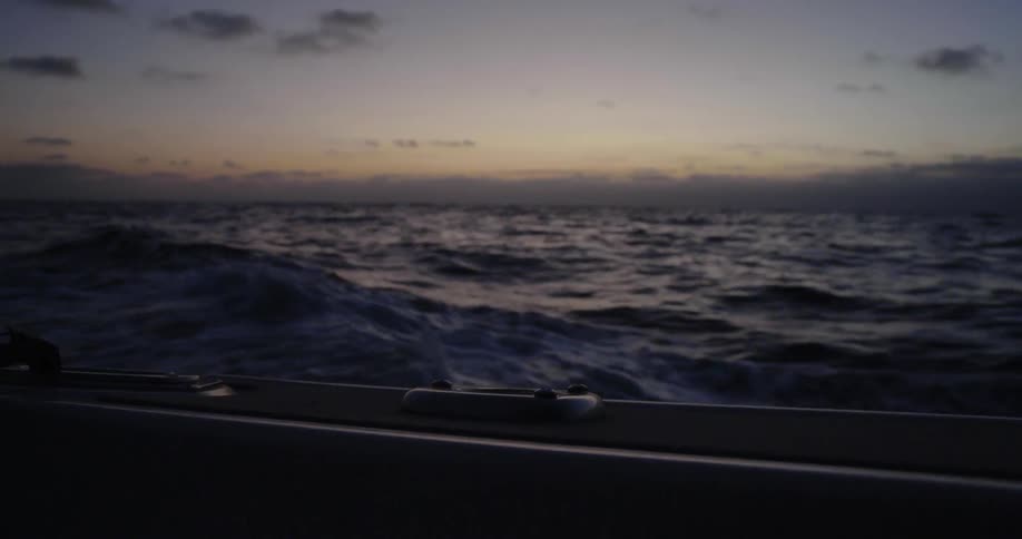 A boat sails on an ocean at sunset