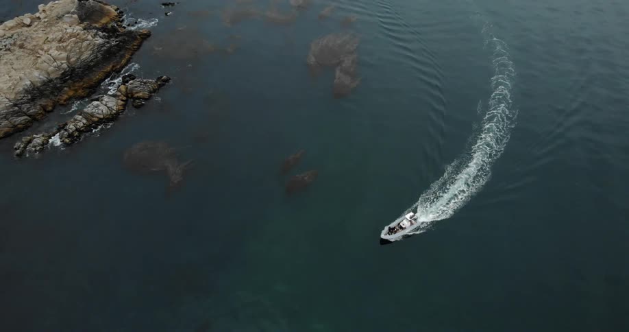 The boat sails around the rocky shore