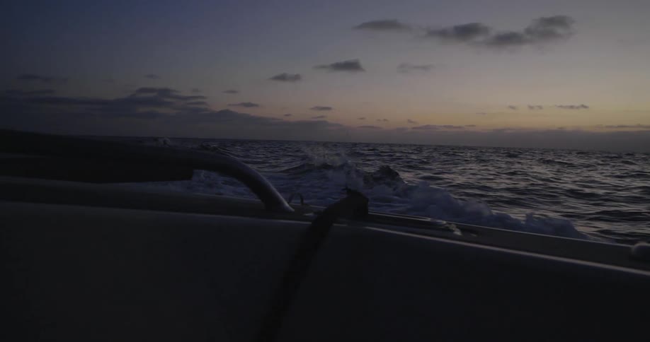 A boat travels through the ocean at sunset