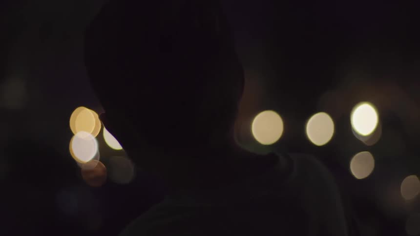 Boy with a camera walking a street at night