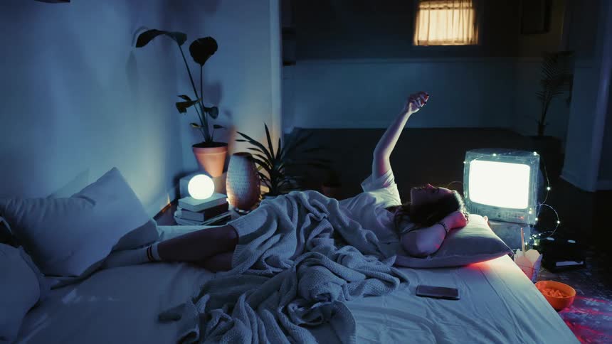 The woman rests in bed while the tv runs