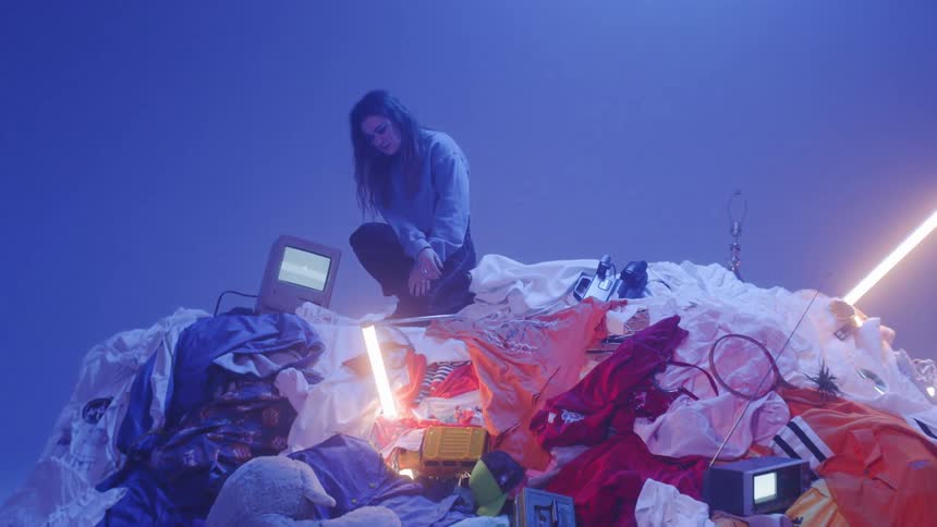 Woman kneeling on a pile of clothes next to small tv