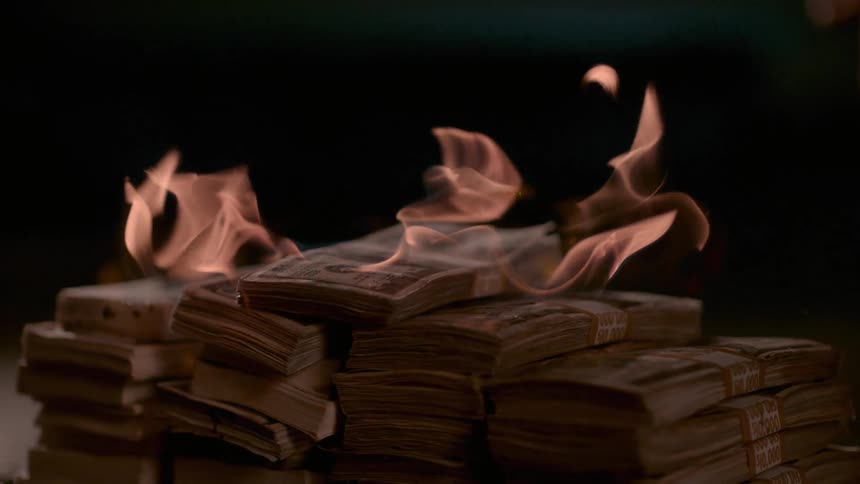 A person drops a bundle of money on fire onto a stack