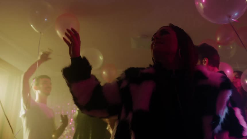 Men and woman dance and play with balloons at a house party