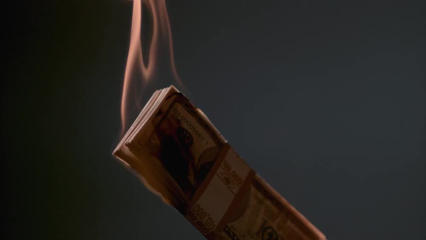 A stack of money on fire in a dark room