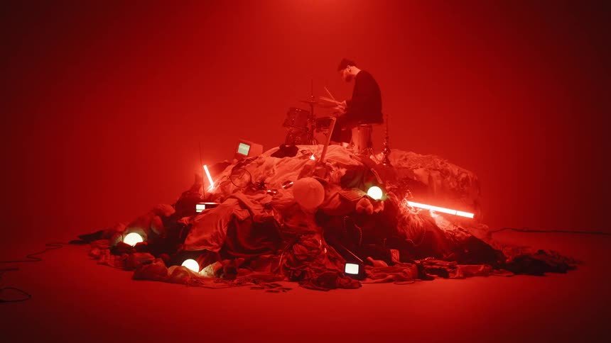 A man plays drums in a dark room with flashing lights