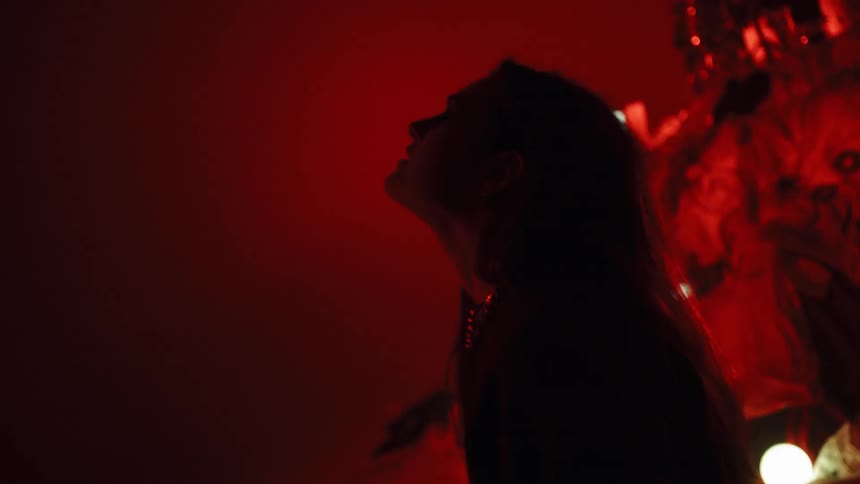 The woman raises her hands above her head under the flashing lights