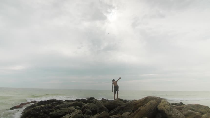 A boy walks on rocks near the ocean