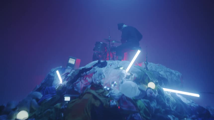 The man is playing drums on the huge pile of clothes