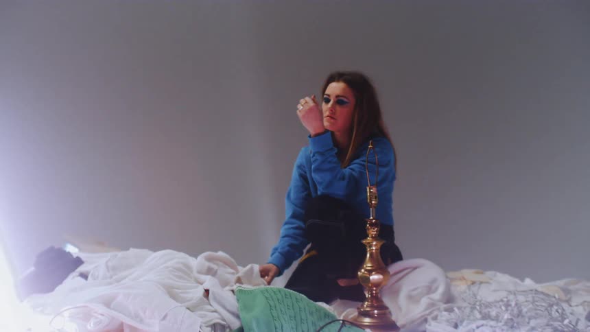 A woman sits on top of a pile of laundry and random objects