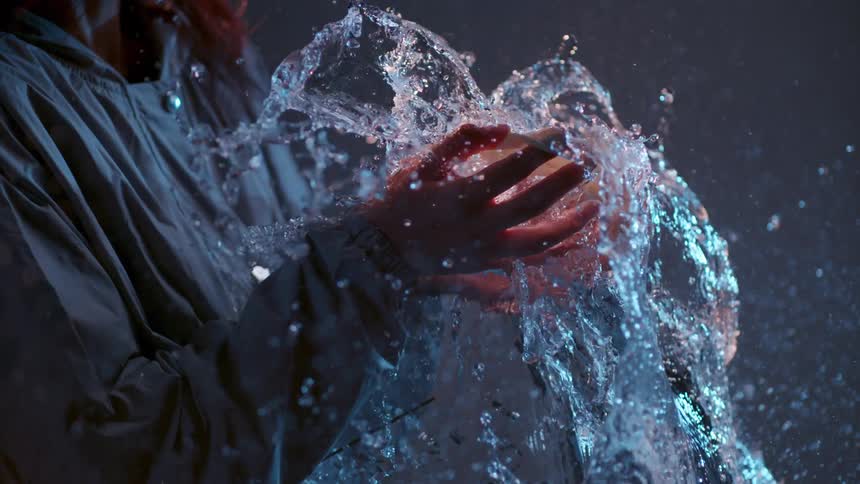The balloon explodes with water in the person's hands