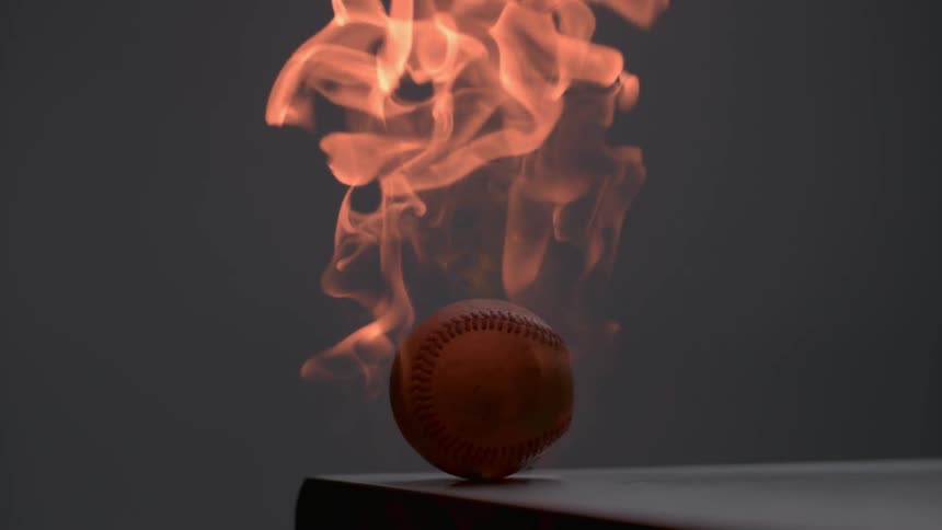 A baseball sitting on a table is on fire with orange flames