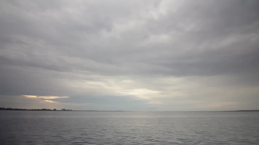 A cloudy sky over a calm ocean with a thin strip of land in the distance