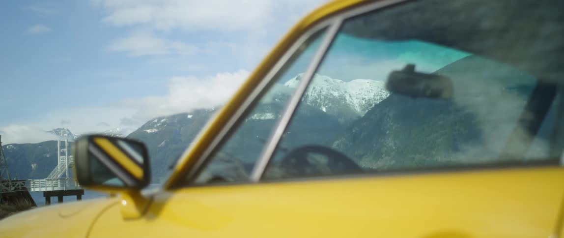 Yellow car is parked near snow capped mountains on cloudy day