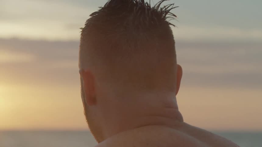 A surfer looks out at a sunset on the ocean