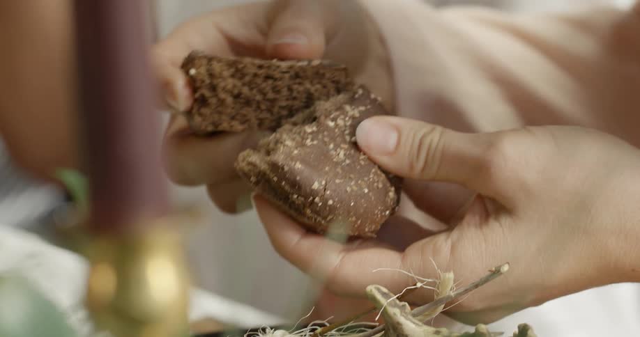 A piece of food is broken in half and one half is handed over