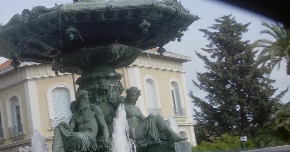 An ornate water fountain flows in a city plaza on a sunny day