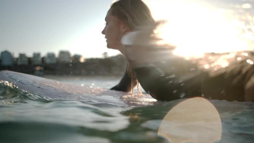 A woman swims on a surfboard in an ocean at sunset