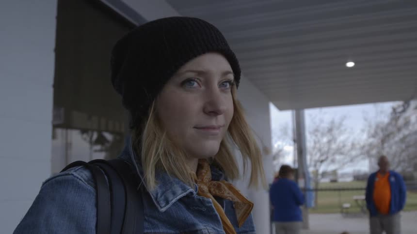 A woman wears a denim jacket and winter hat while waiting outside