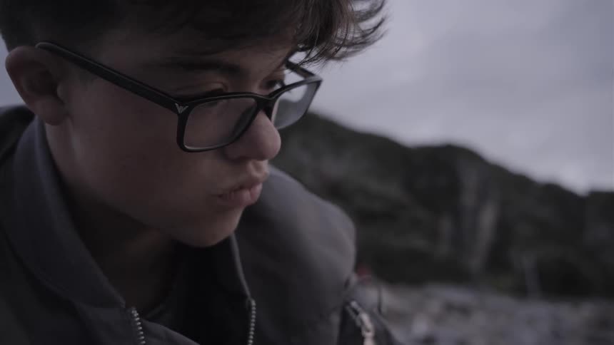 A boy wears glasses outside on a cloudy day