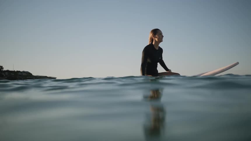 A woman floats on a surfboard in an ocean