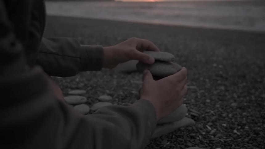 A man holds some rocks sitting on the beach