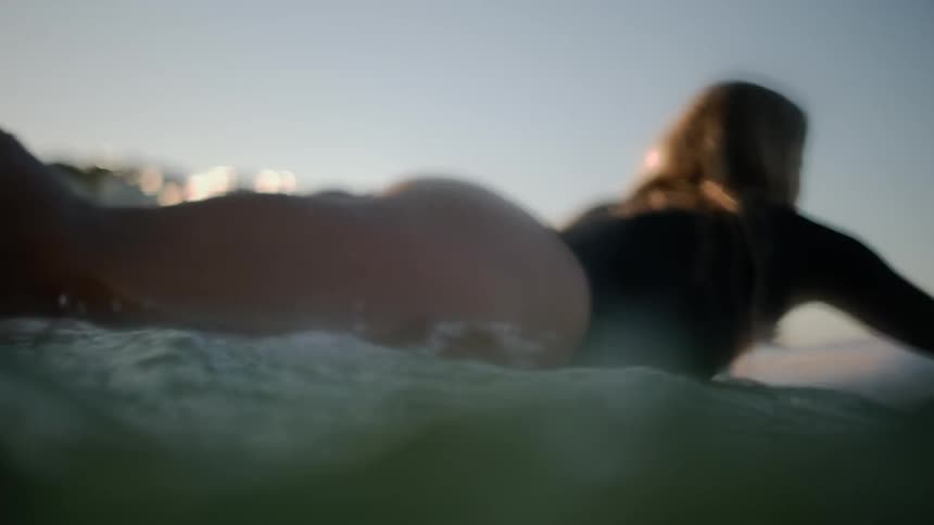 A woman swims on a surfboard in an ocean at sunset