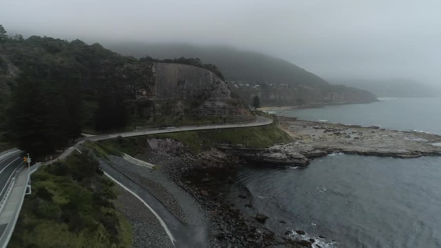 Cars travel on a coastal road on a foggy day