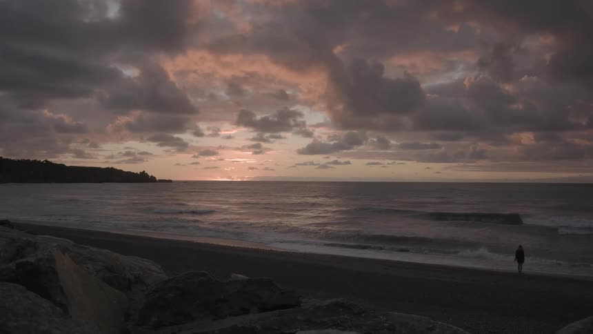 A person walks on a beach at sunset