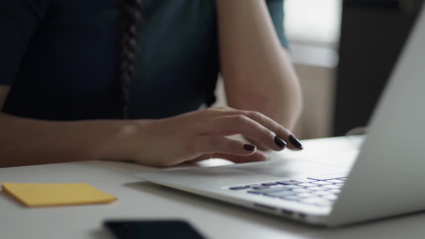 Woman with painted nails scrolls on a laptop
