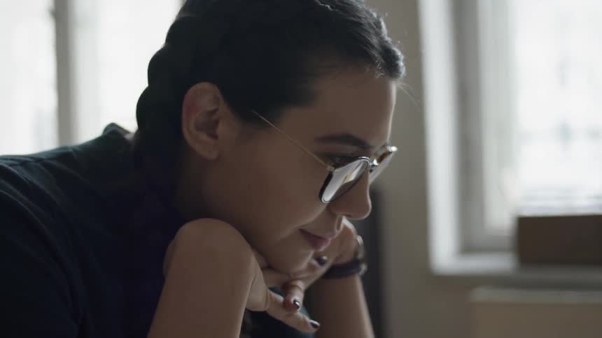 A woman wears glasses while deep in thought at a desk