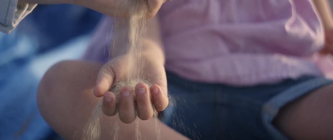 A young girl has sand poured into her hand