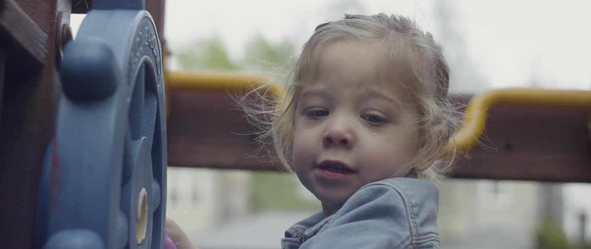 Child turns the wheel while holding a doll in her right hand
