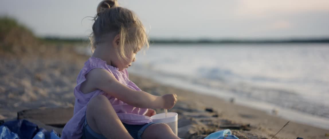 A young girl puts wet sand into a cup on the beach