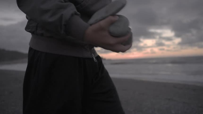 The man kneels down with rocks on the beach