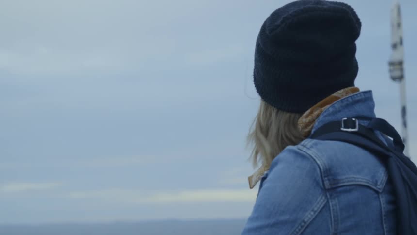 A woman leans on the railing and looks out at the ocean then turns and smiles