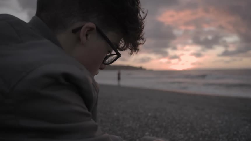 A man sits on a beach at sunset