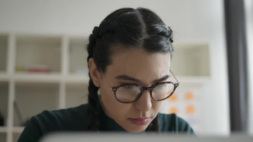 A woman in glasses works on a laptop