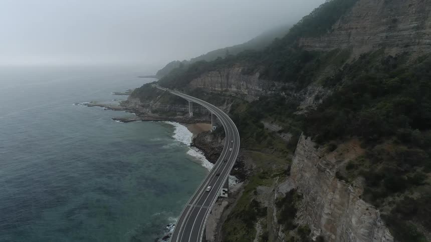 Vehicles travel down the winding road near the ocean
