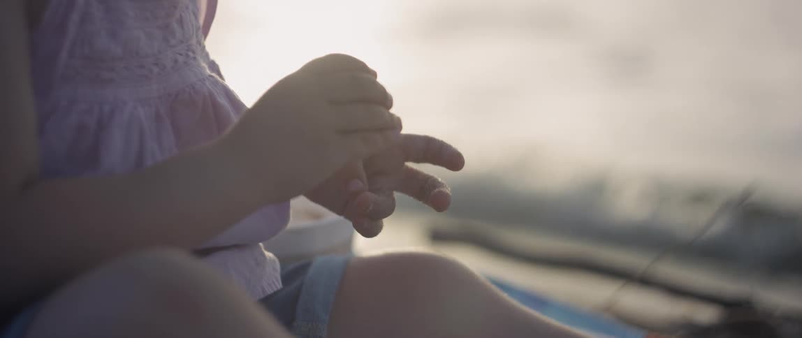 A young child plays in sand on a beach at sunset