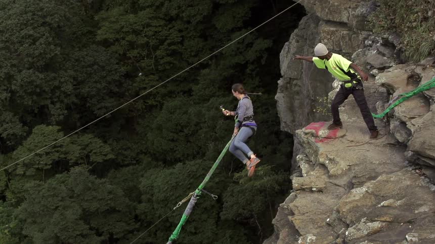A woman bungee jumps close to a mountain