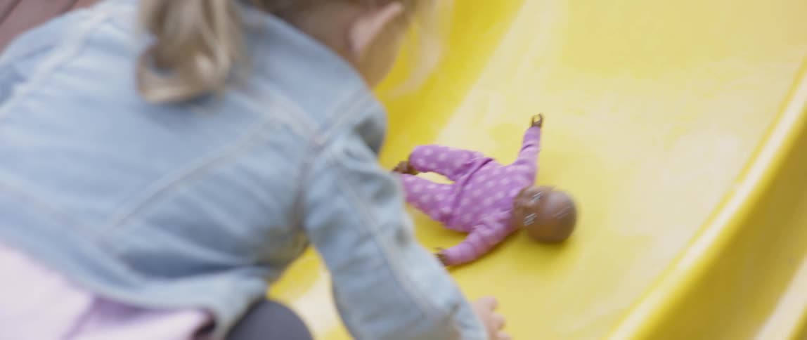 The child is pushing her doll up the slide