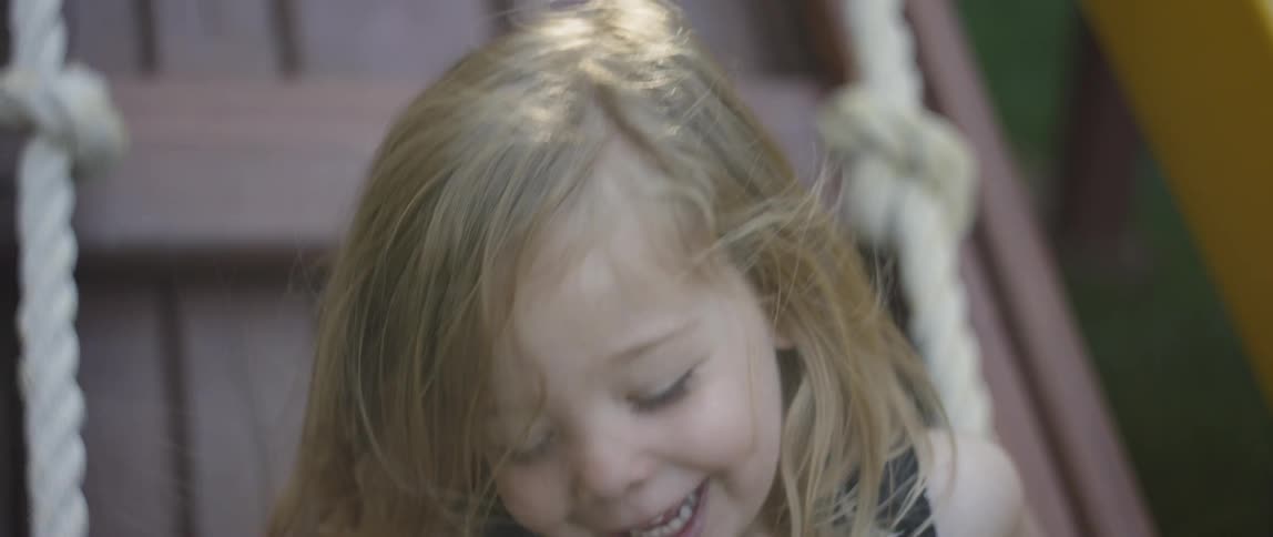 A young girl laughs as she holds onto a white rope