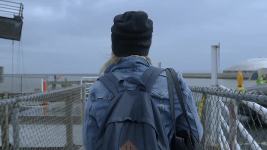 A woman adjusts her bag as she walks toward passing cars on the dock