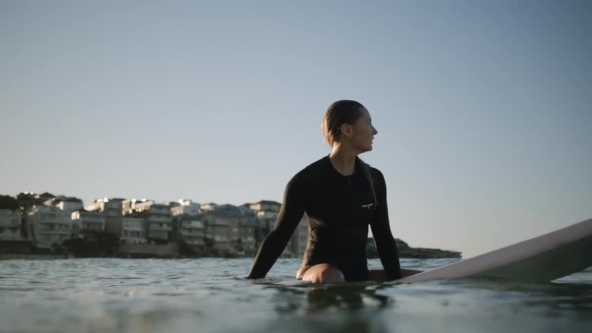 Woman sits on a surfboard in the ocean under a blue sky
